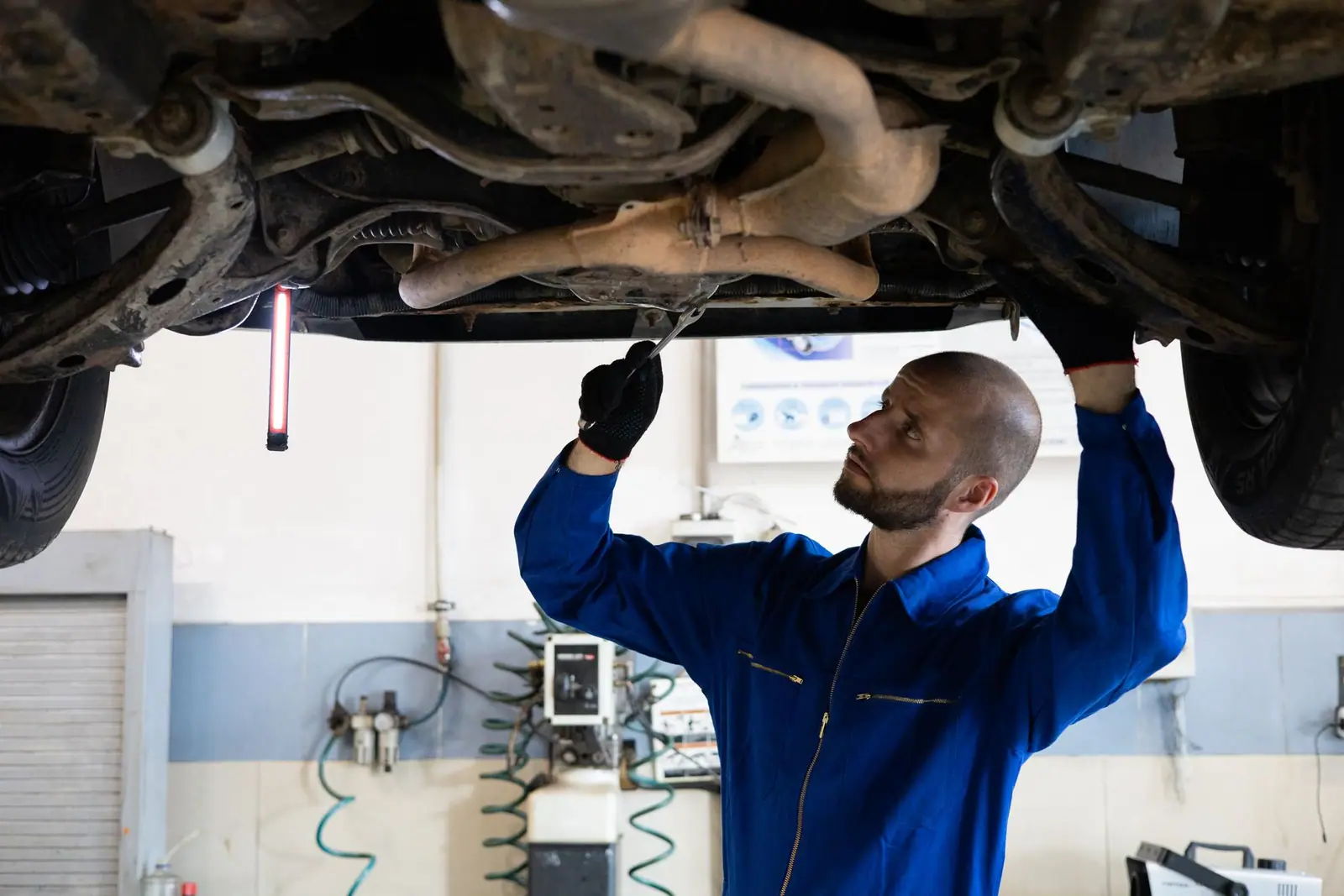 A mechanic in blue coveralls inspecting the underside of a raised car