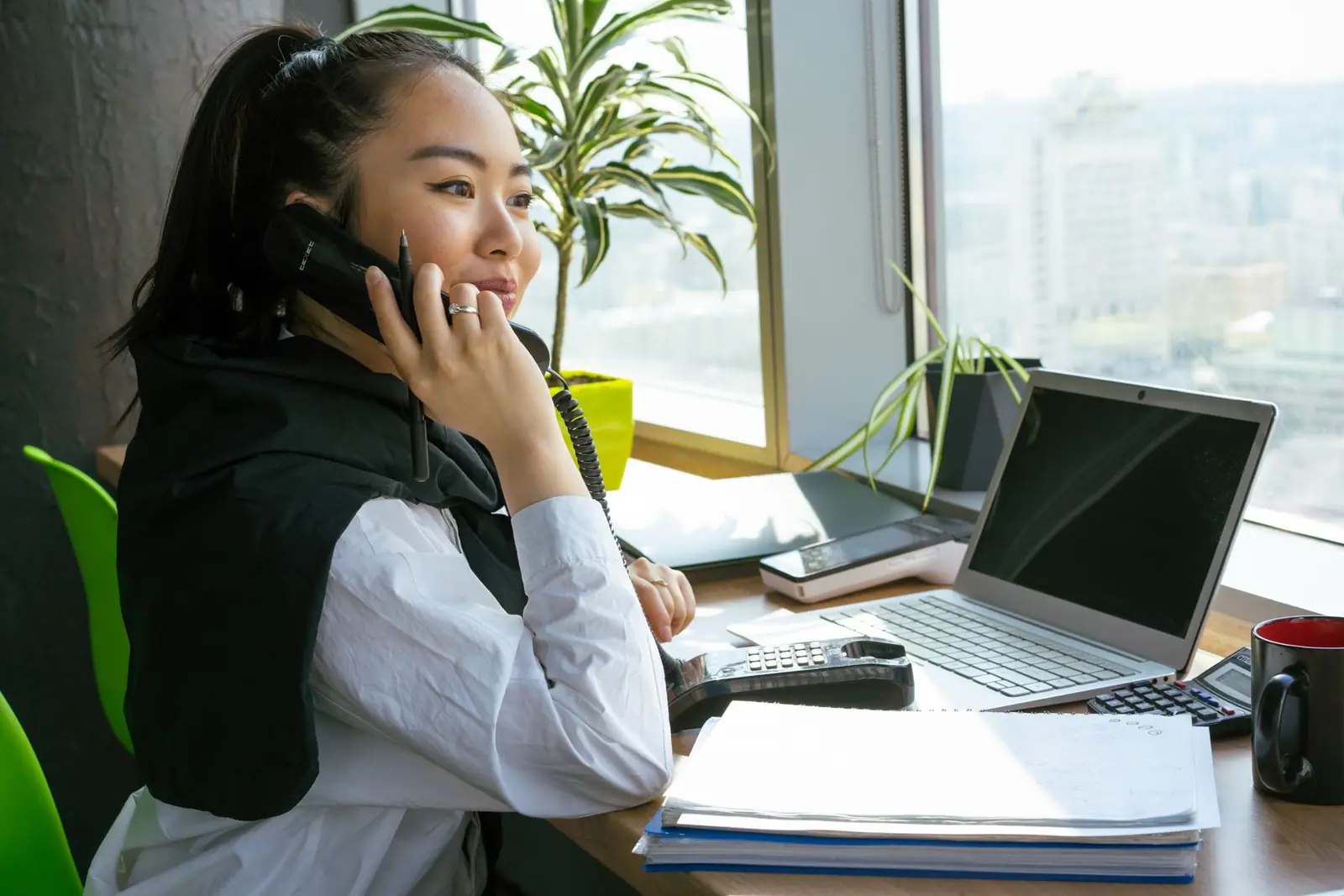A woman speaking on a phone beside a laptop and papers