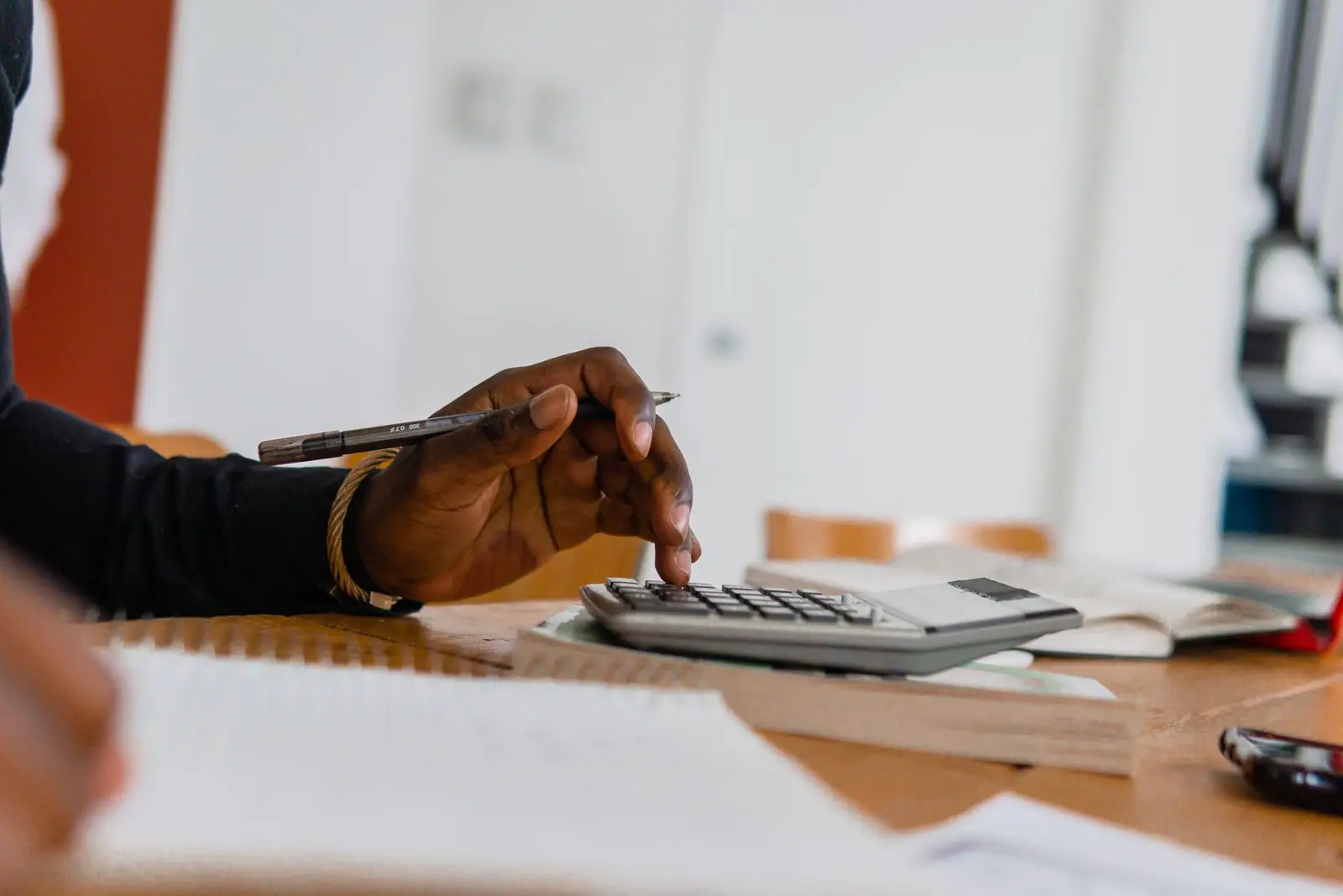 A hand holding a pen beside a calculator and papers on a desk