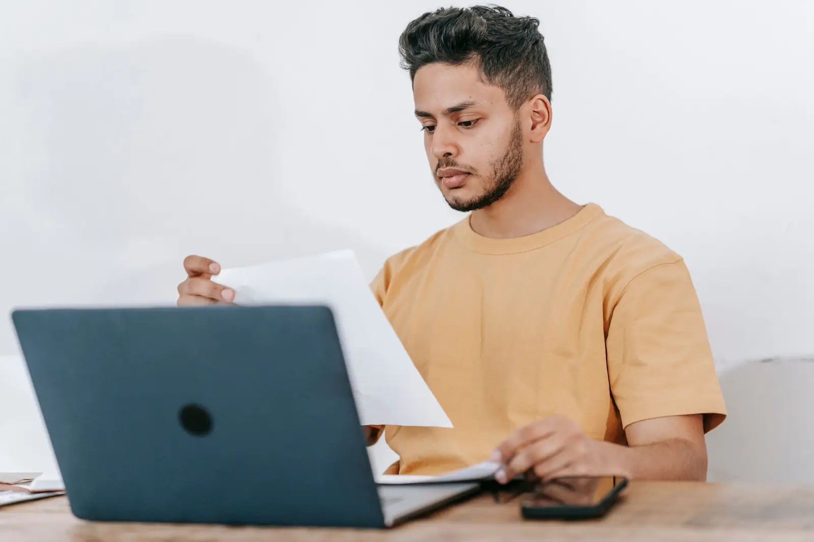A man reading a paper beside an open laptop