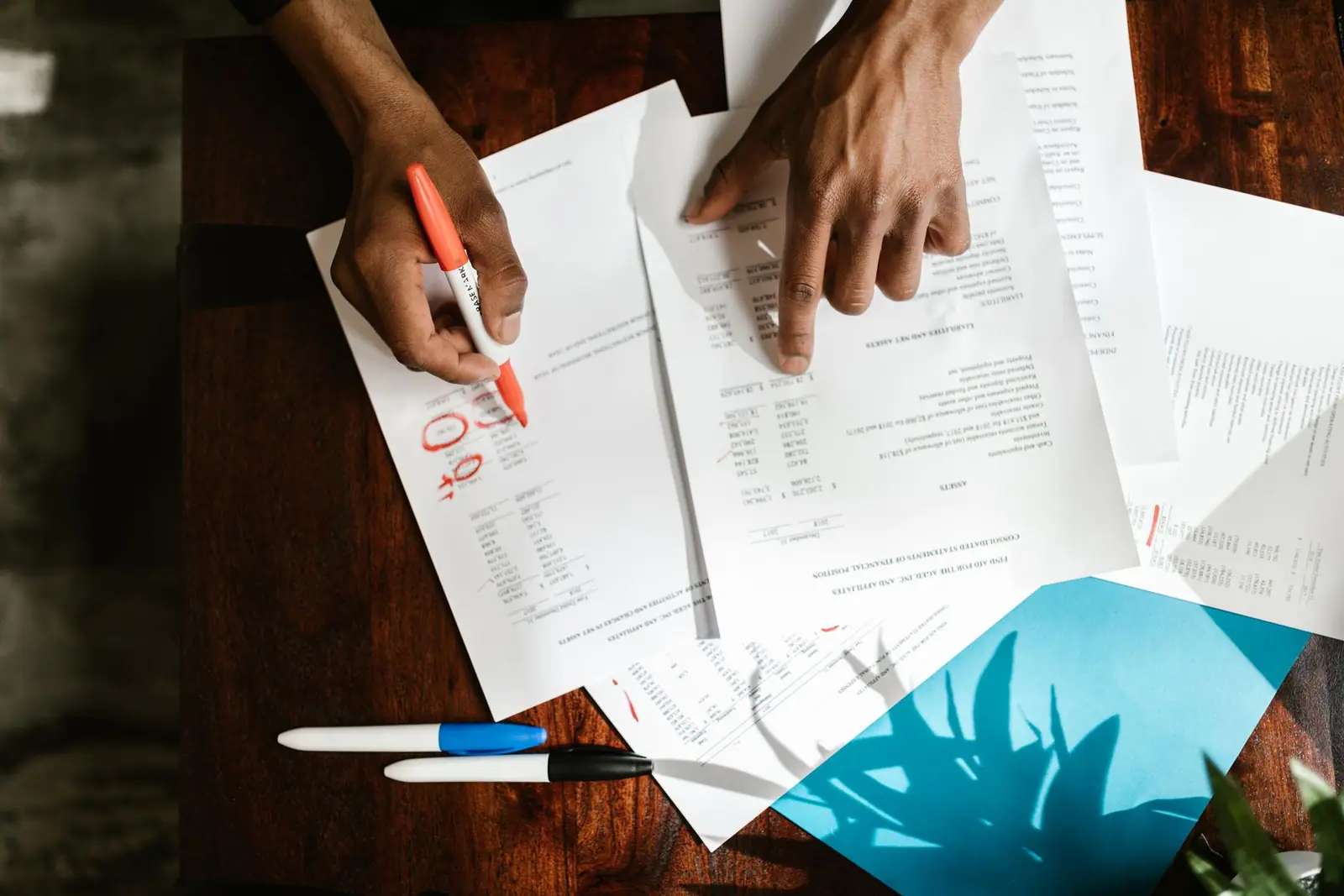 Hands marking figures on printed documents on a desk