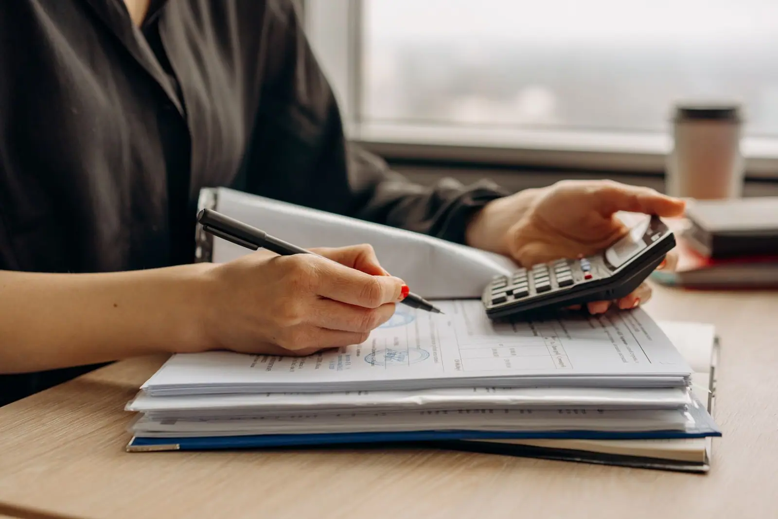 A person using a calculator beside paperwork on a desk