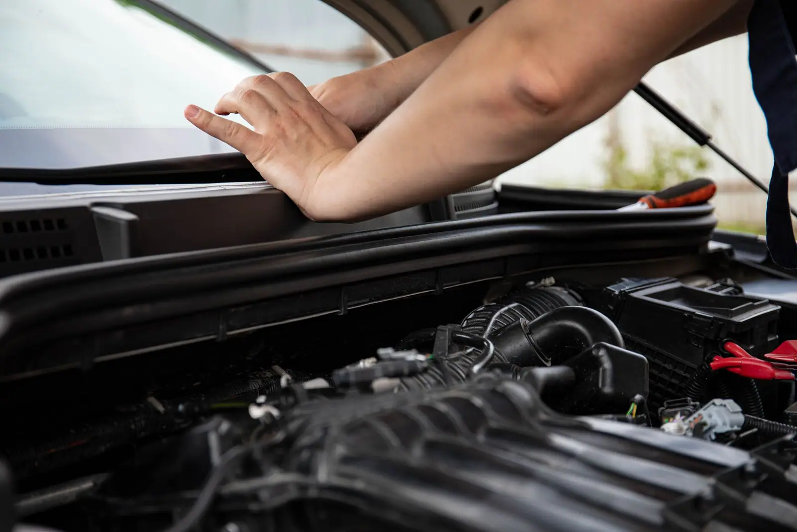 A person resting a hand on a clipboard above an open car engine compartment