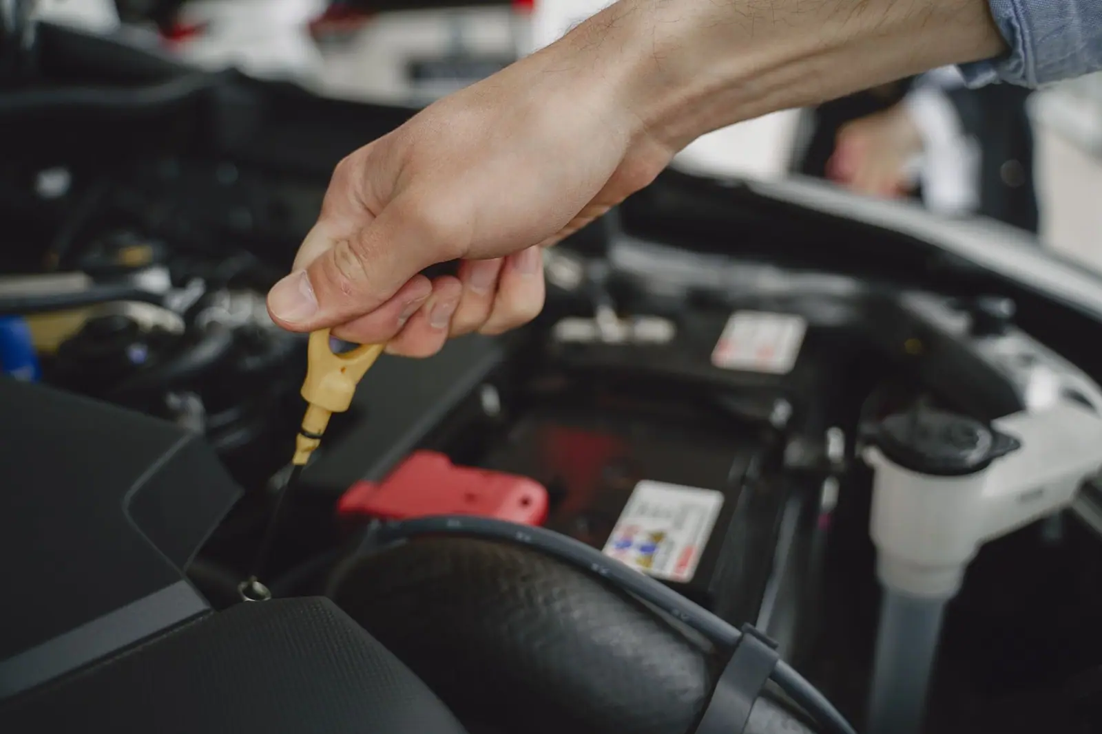 A hand holding a yellow oil dipstick in an engine bay