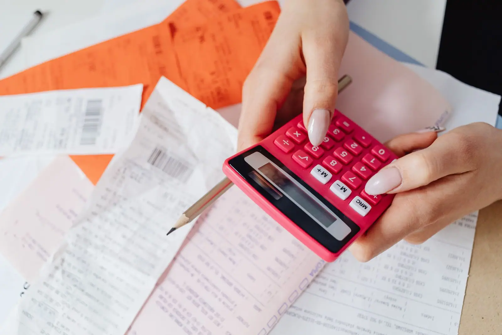 Hands holding a pink calculator over papers