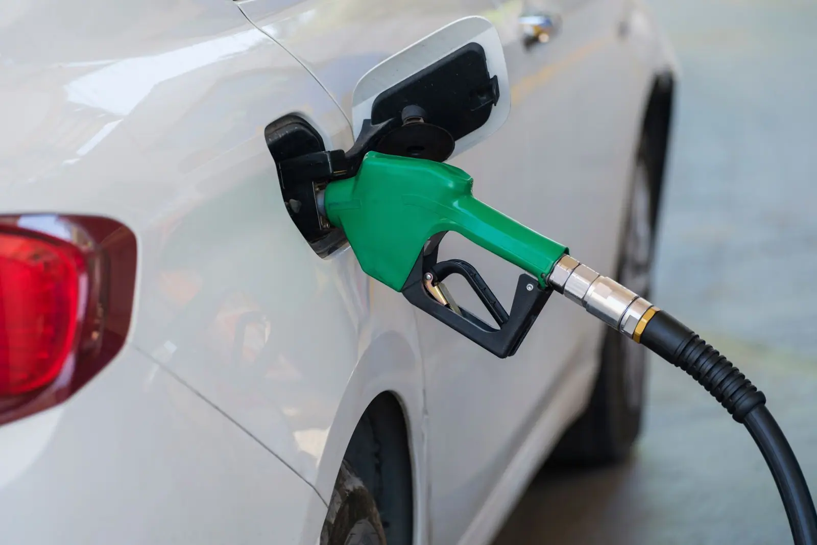 A green fuel pump nozzle filling a white car