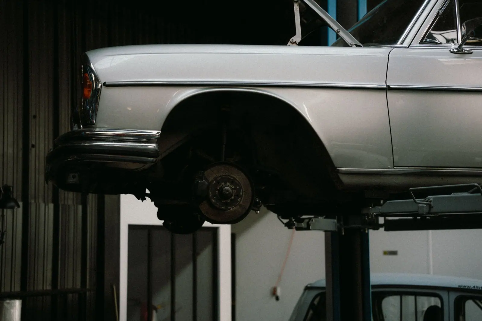An older silver car raised on a lift with a wheel removed