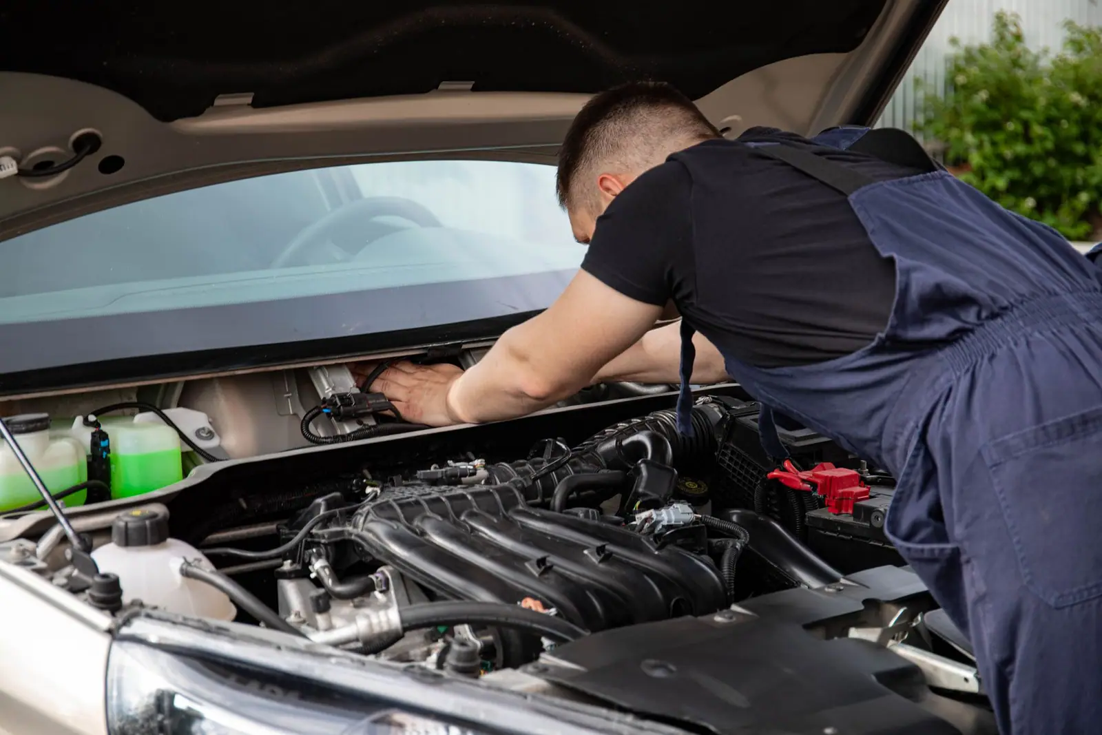 A mechanic leaning over the engine bay of a car with the bonnet raised