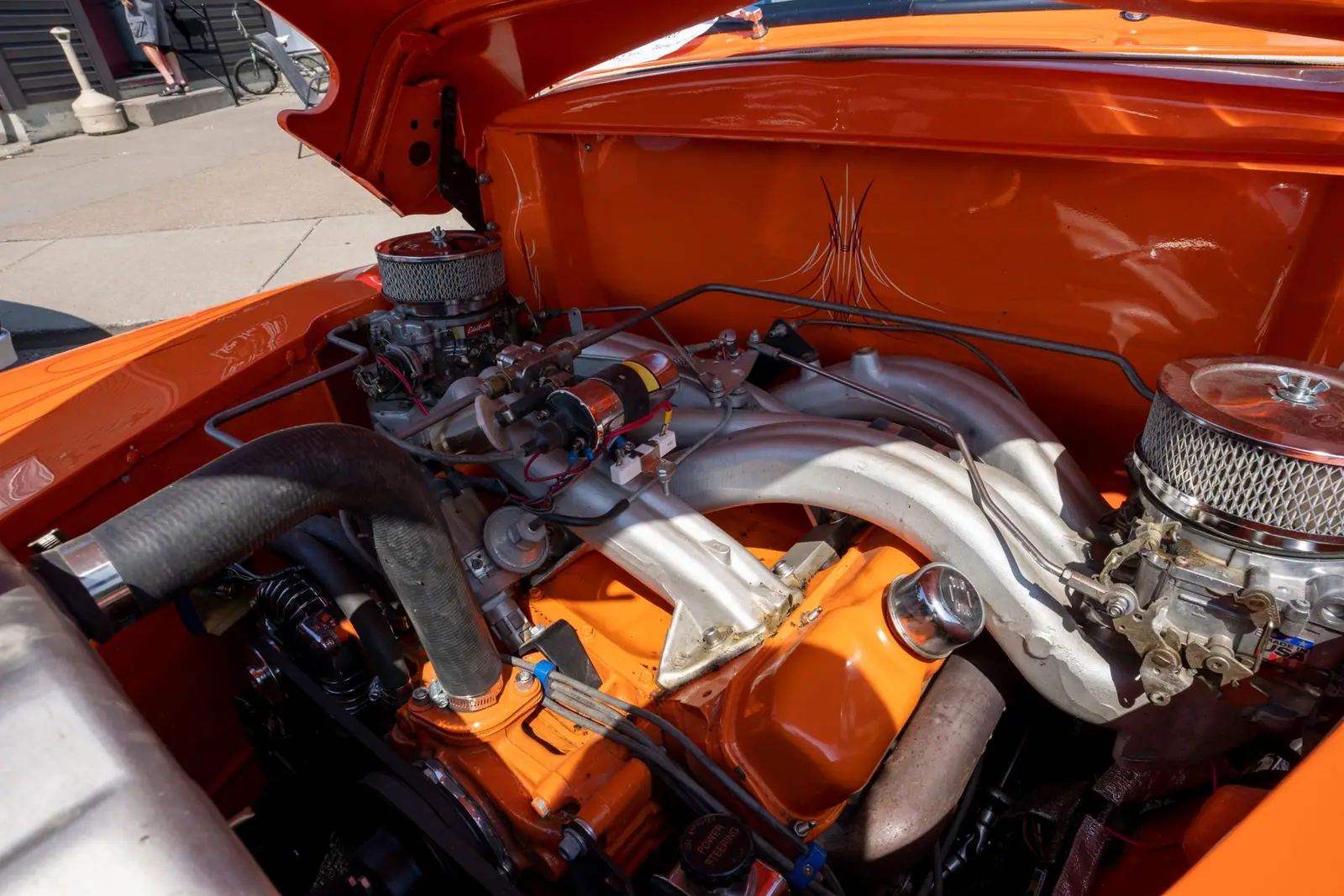 An orange classic-car engine compartment with hoses and metal components