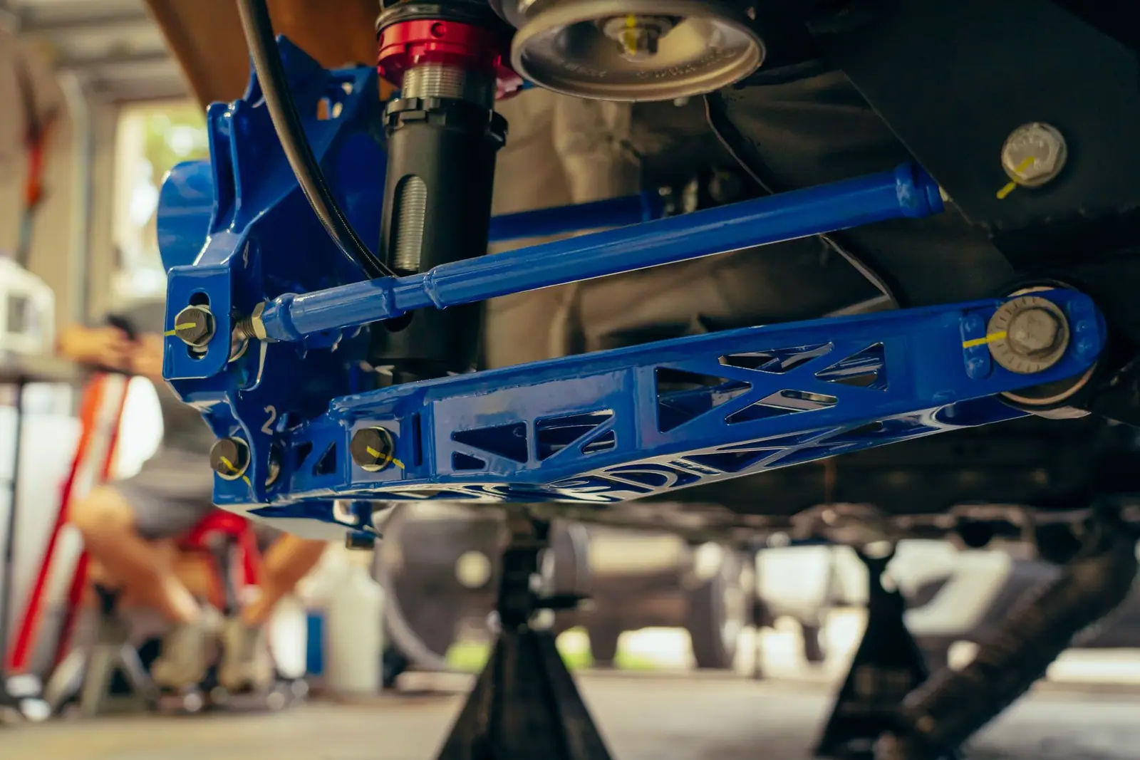 Blue suspension arms and a coil spring assembly beneath a raised vehicle